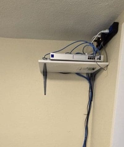 Network equipment sitting on an open shelf with exposed cabling and power outlets at the Garyland cottage before the cabinet upgrade